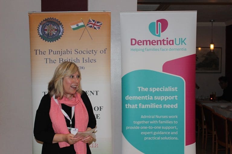 Brenda Foulds speaking at a presentation in front of a Dementia UK banner