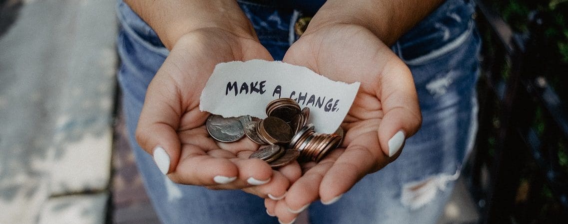 A pair of hands holding coins and a scrap of paper reading 'make a change'