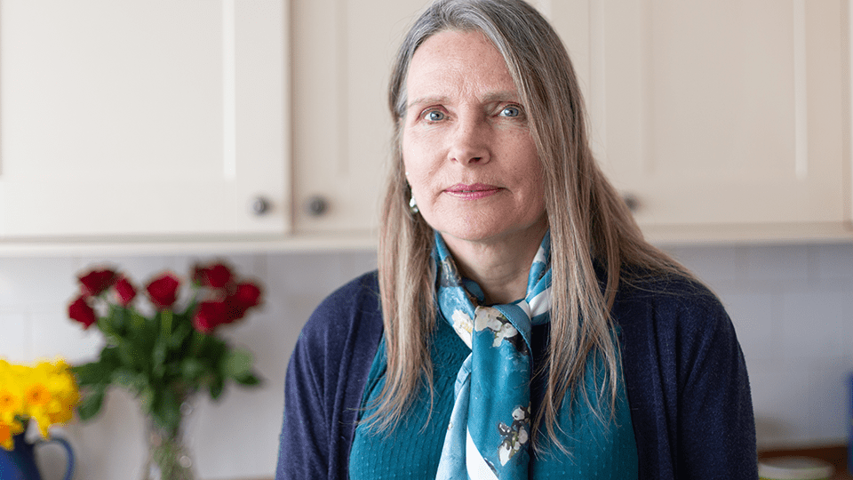 Janet stands in her kitchen with flowers in the background