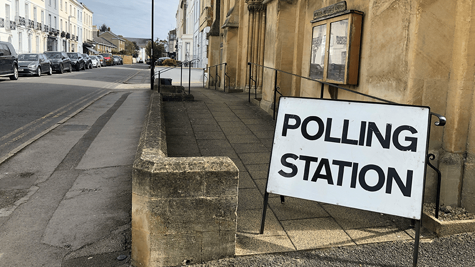 A polling station sign stands outside a city hall