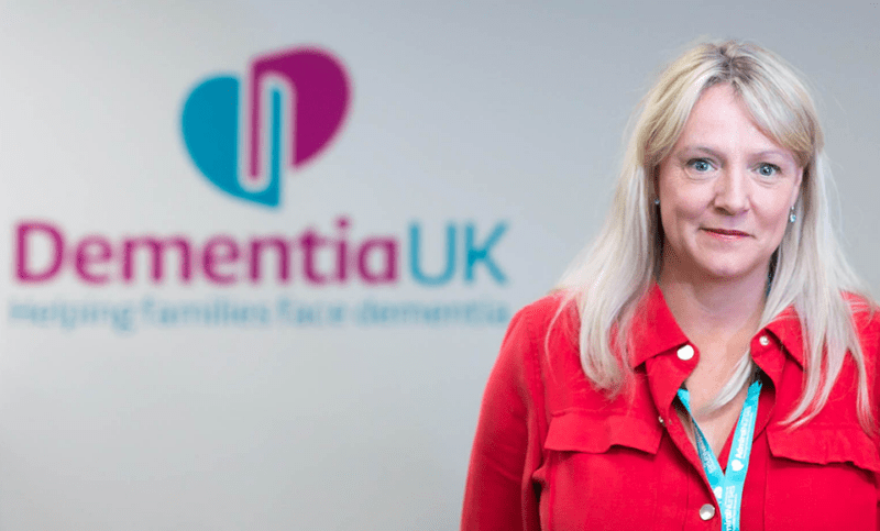 Helen McDavitt stands in front of the Dementia UK logo