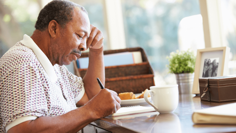 Man sitting at a table writing on a piece of paper