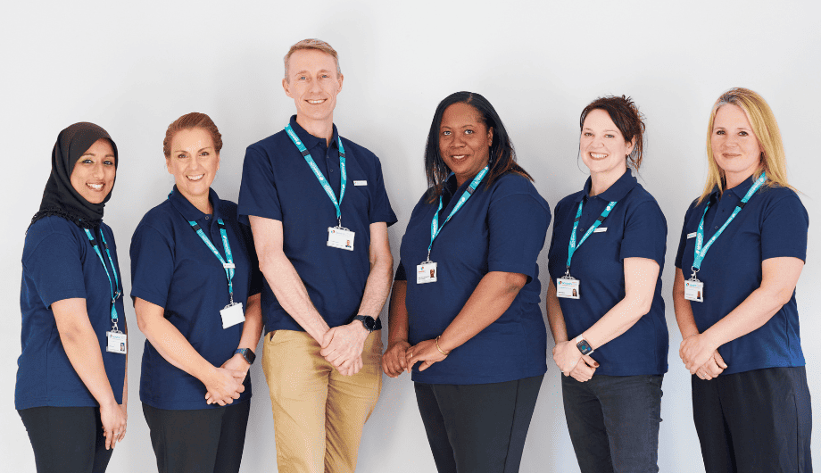 Two female Admiral Nurses on left, male Admiral Nurse in the middle, three female Admiral Nurses to the right. All wearing blue polo neck tshirts and Admiral Nurse landyard