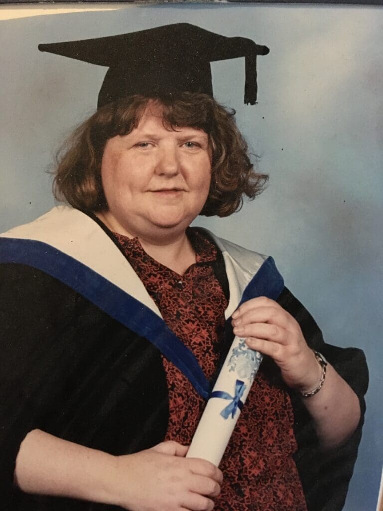 Julie holds her graduate certificate wearing a graduation gown