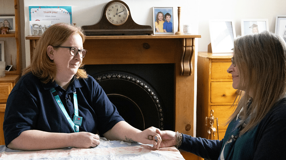 Admiral Nurse Jody holds Janet's hand across the table