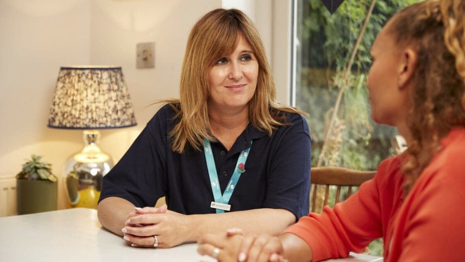 Emma Dougal, Admiral Nurse talks to a female carer at home in her garden.