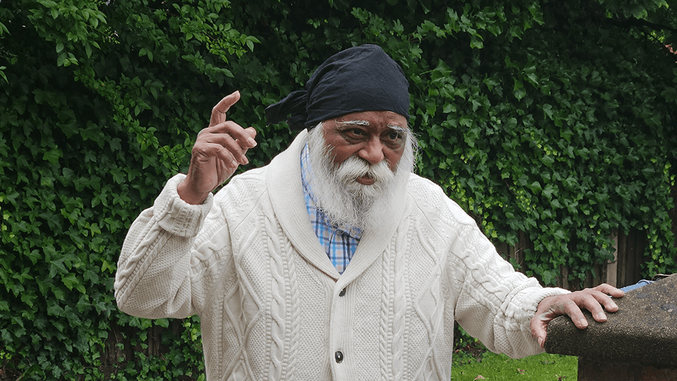 Mohinder stands in the backyard with his right hand raised while speaking