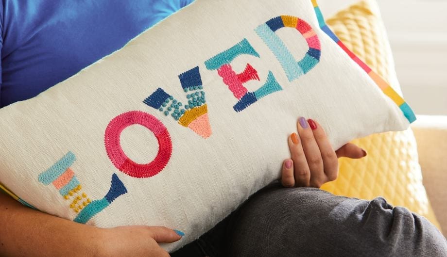 Dementia UK and Next collaboration cushion with the word Loved emboidered on it in rainbow colours.