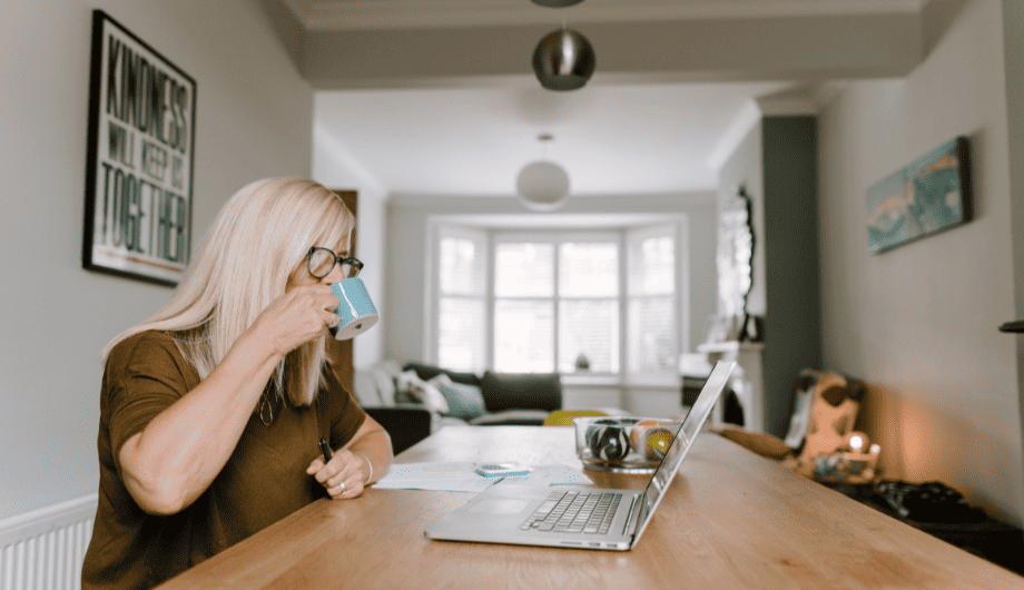 Lady drinking a cup of tea whilst reading her laptop in front of her