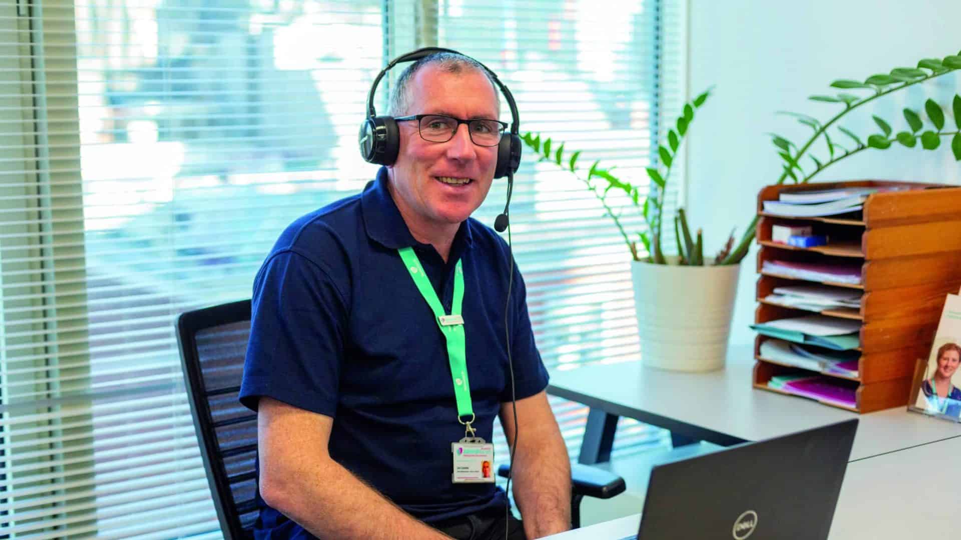 Admiral Nurse Joe Costello, sitting at a desk with a headset on and looking at a laptop