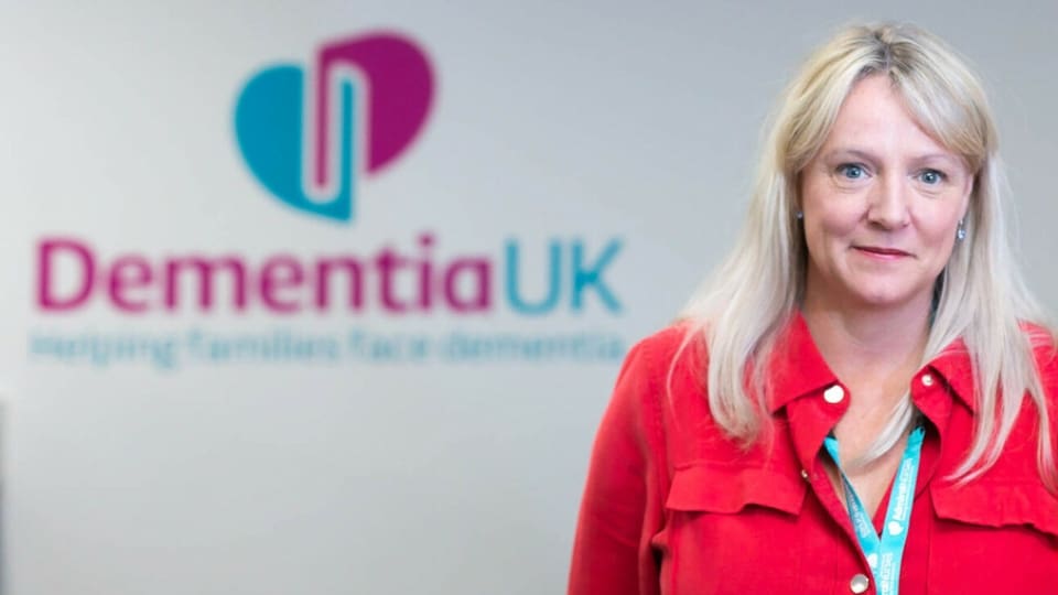 Helen McDavitt stands in front of the Dementia UK logo