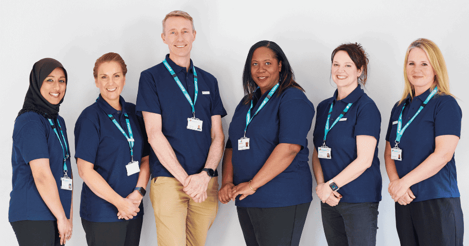 Two female Admiral Nurses on left, male Admiral Nurse in the middle, three female Admiral Nurses to the right. All wearing blue polo neck tshirts and Admiral Nurse landyard