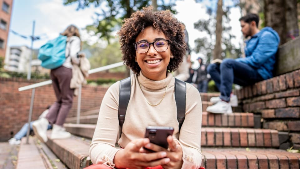 Teenager sitting on some steps outdoors texting and smiling