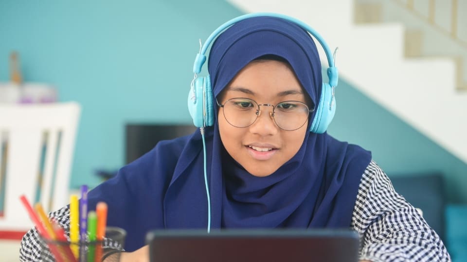 a child wearing headphones is using their laptop