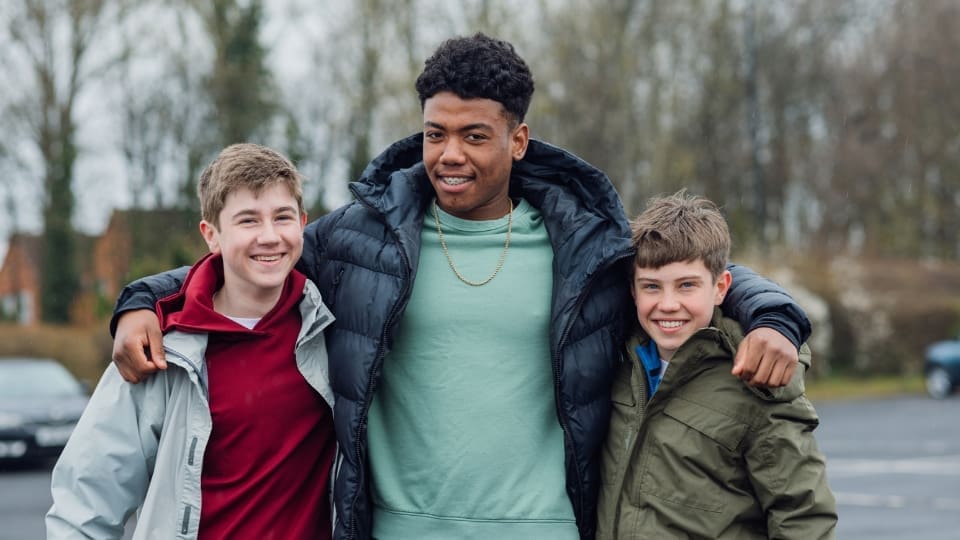 teenager standing between two children with their arms wrapped around both of them