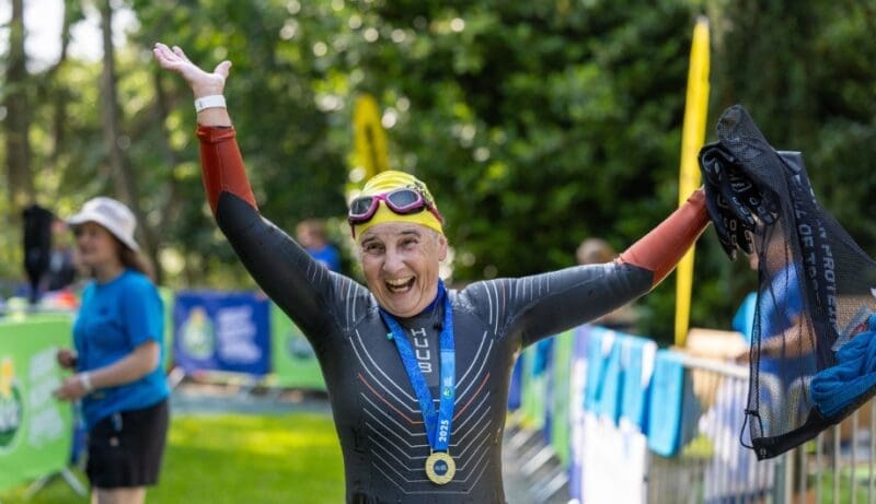 supporter wearing a medal and raising their arms to celebrate completeing the great north swim