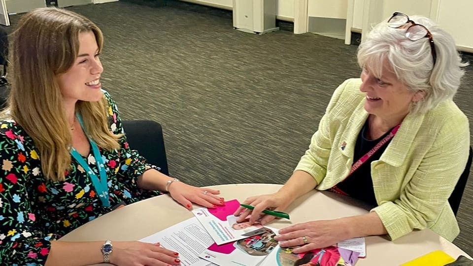 MP Caroline Voden with Beth from our campaigns team sat together at a table talking and smiling