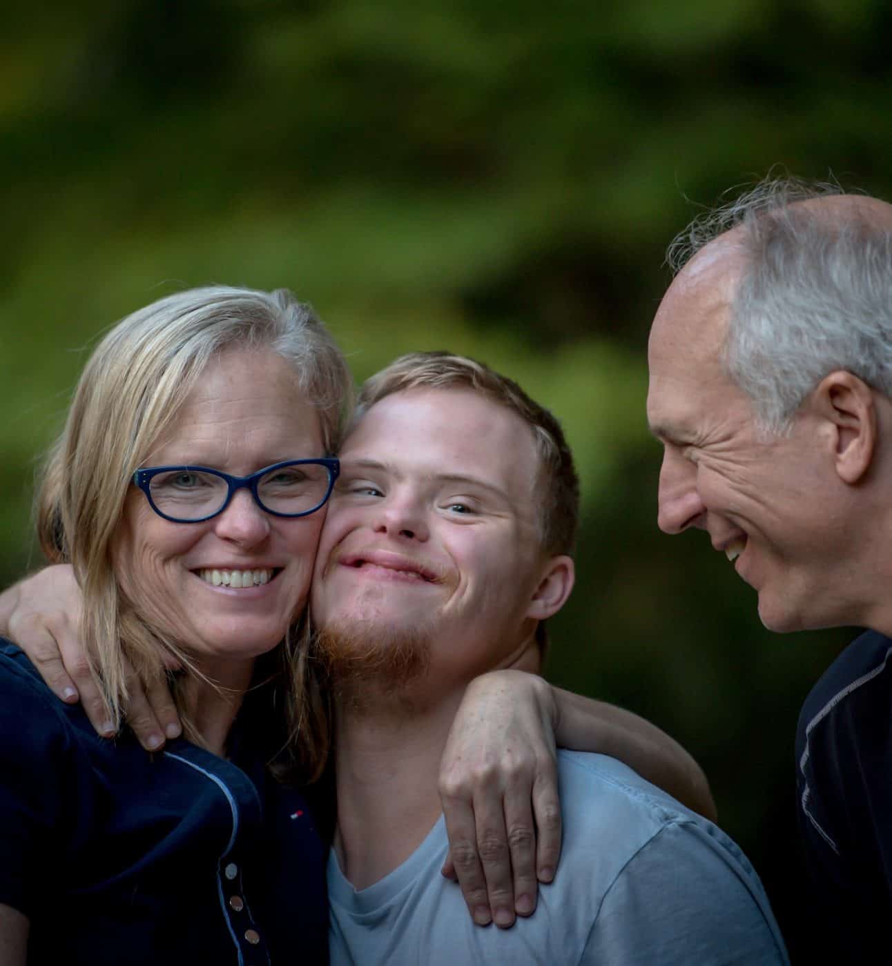 A boy smiles, flanked by two close relatives