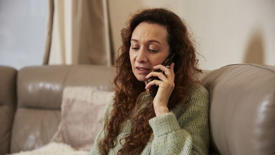 A woman calls the Helpline at home on her sofa.